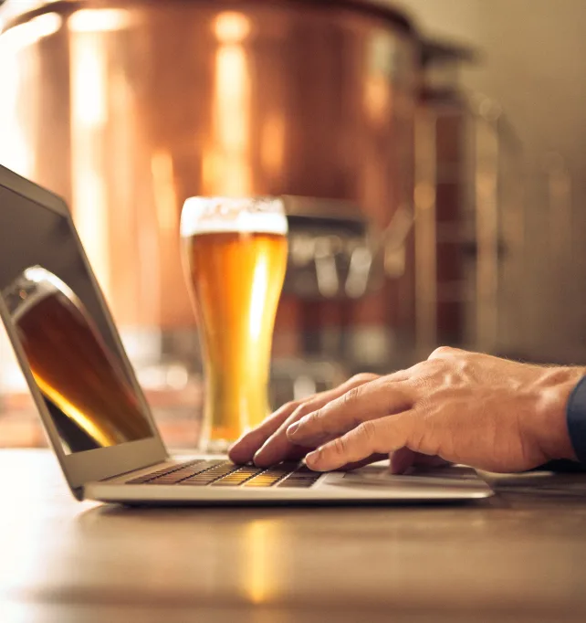 Notebook sendo usado em uma cervejaria com um copo de cerveja ao fundo